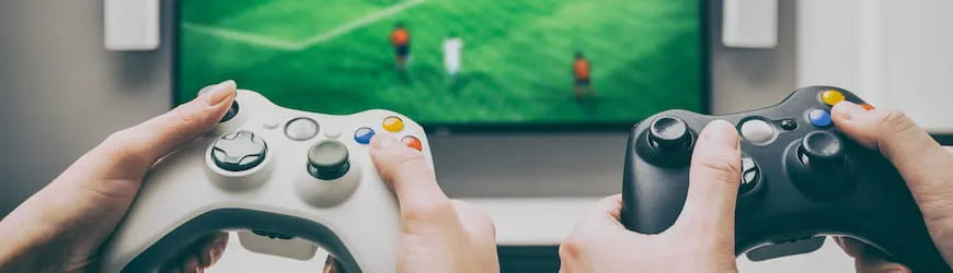 Des mains qui tiennent des manettes de jeu vidéo, devant un écran de jeu de foot : un jeu qui exige des compétences en coopération et pensée stratégique. 